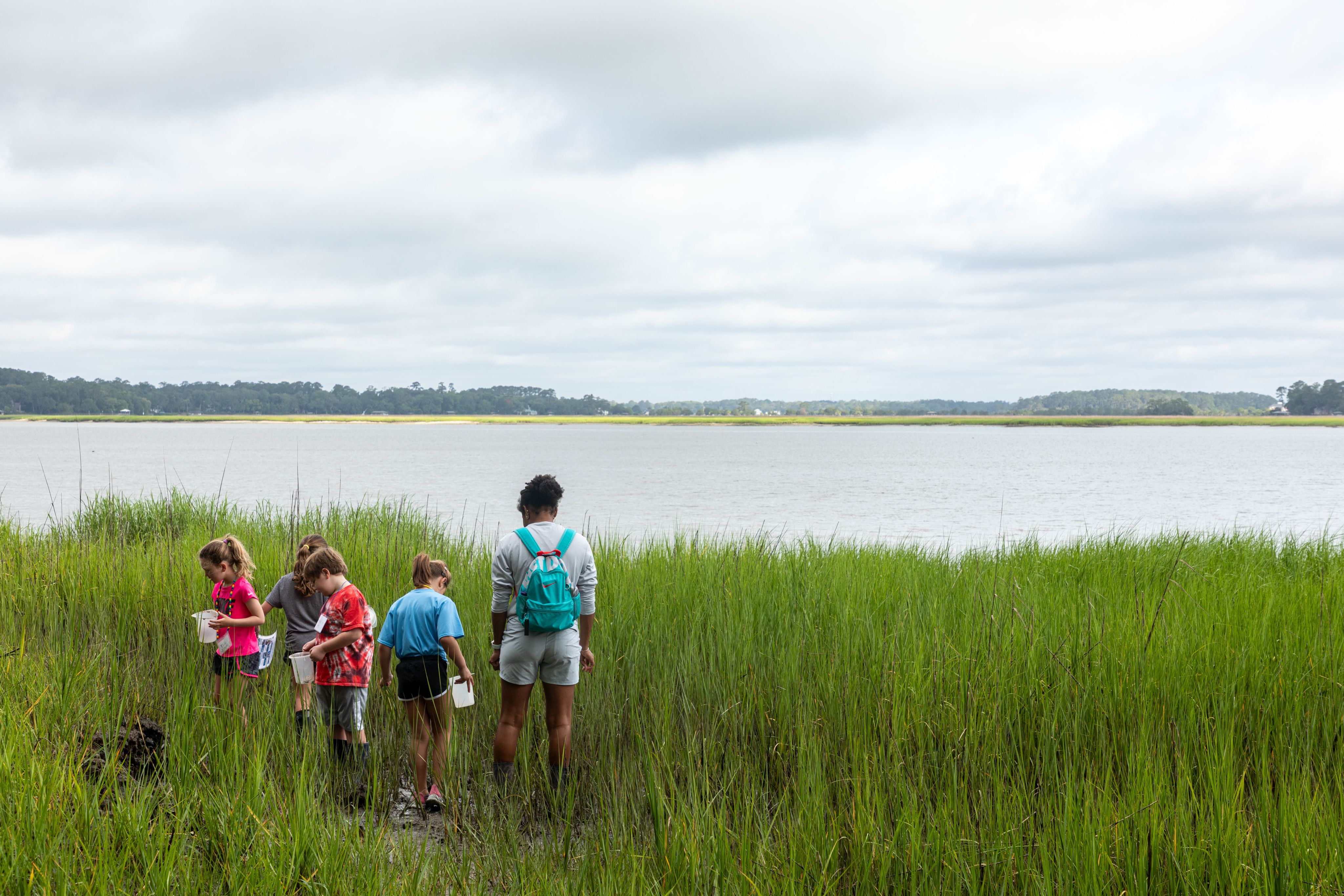 Marine Educator in the marsh with kids, their backs are facing the camera and they are looking out over the Skidaway River
