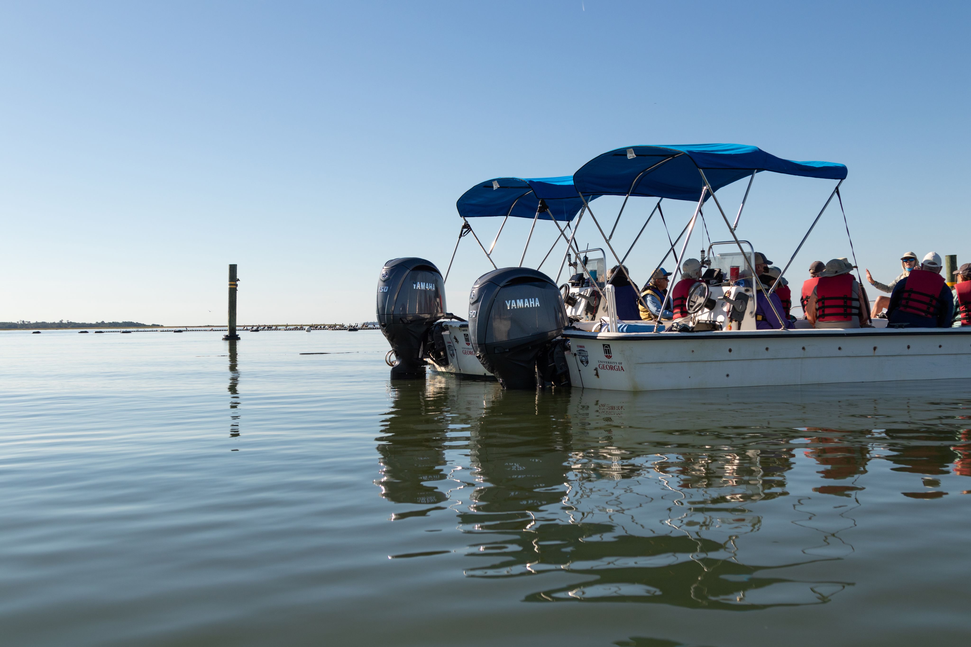 Two Marine Extension and Georgia Sea Grant skiffs in the water with Yamaha motors shown. A marine educator is on board teaching a group of public program participants