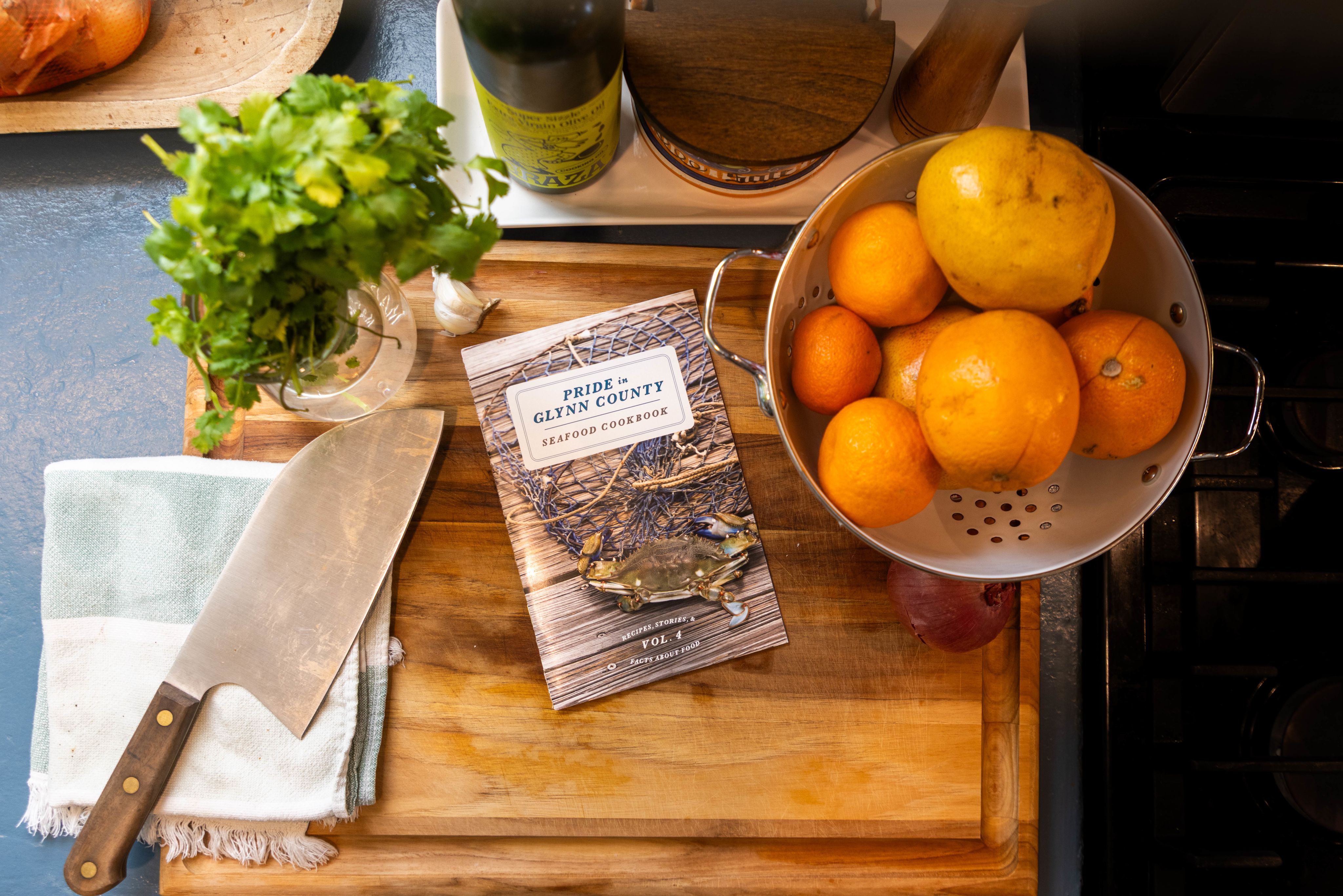 A Pride in Glynn County Seafood Cookbook laying on a cutting board next to a knife and various ingredients in a residential kitchen.