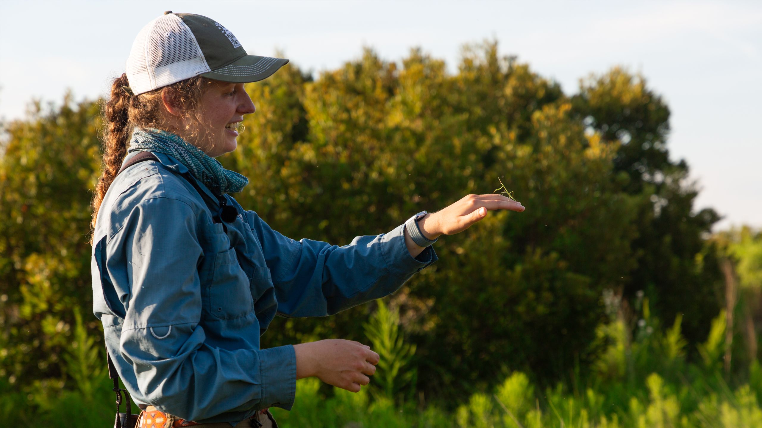 REsearcher holding a praying mantis on her hand in a wooded environment