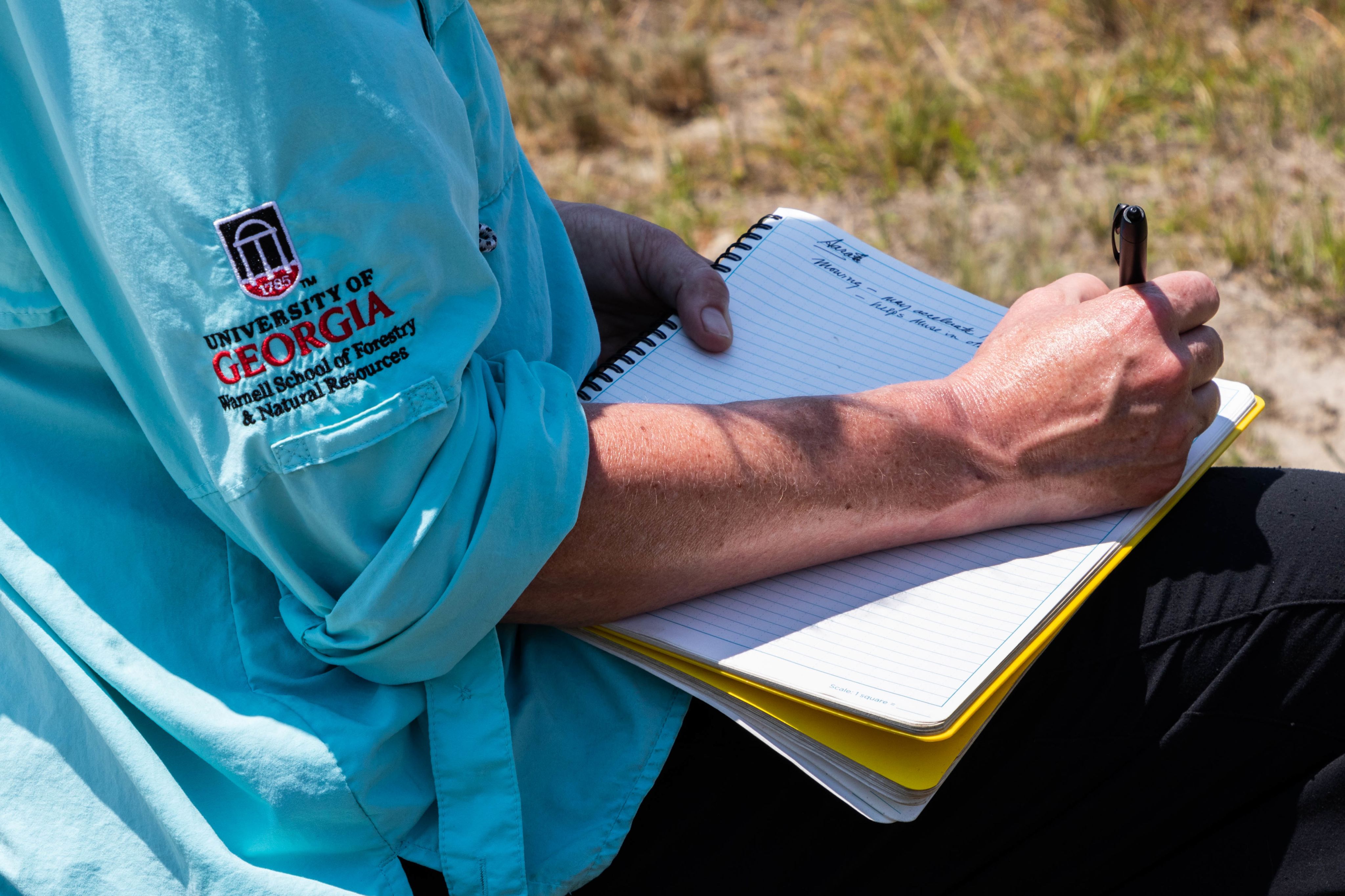 a close up of someone writing in a notebook while outside